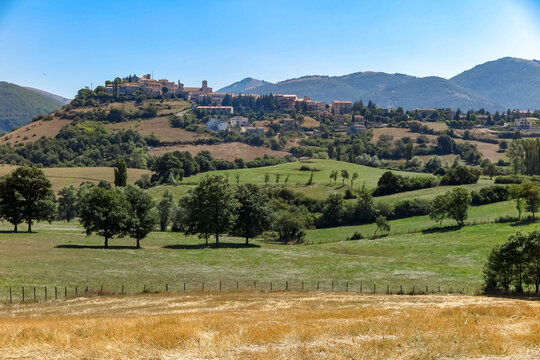 Old Italian commune, on top of a hill with lawn and trees around it and mountains in the background, Monteleone di Spoleto, Umbria region, province of Perugia, Italy