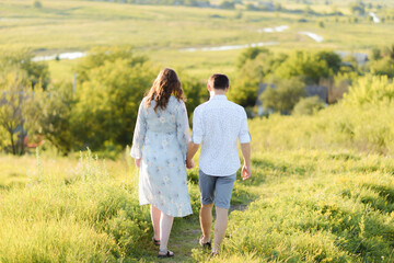Pregnant woman holding hands with her husband during a walk in the field at sunset. Happy family and newborn.
