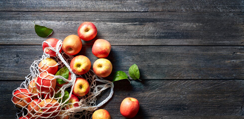 Red apple and string bag on wooden background. Ripe apples on vintage table and copy space. Summer or autumn season.