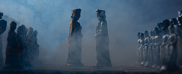 stylized chess pieces on a board with black background, smoke and selective focus