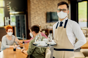 Portrait of a happy waiter with protective face mask serving coffee in a cafe.