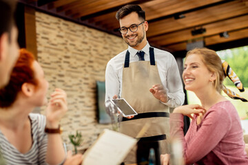 Young happy waiter taking order from his guests in a cafe.