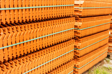 Red roof tiles are packed in standard packaging on building pallets for further transport.