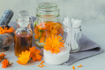 Natural cosmetic oil, a tincture or infusion, cotton pad, sticks and towels with Calendula flowers on light background. Healthy skin care. Aromatherapy, spa and wellness concept