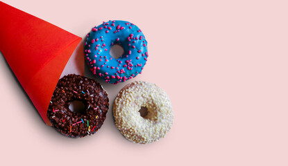 Sweet delicious doughnuts in chocolate, blue and white glazes fall out of a red bag on a light background. Free space for copying. Donuts as a delicious snack, sweet pastry dessert.