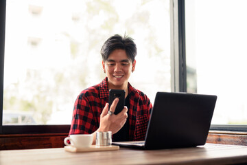 Happy young handsome Asian hipster man using phone and laptop at the coffee shop - Powered by Adobe