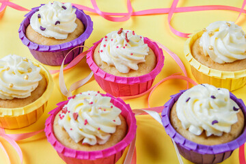 Four multi-colored cupcakes with cream on a yellow background with different ribbons. Festive background with free space. Holiday baking. Birthday baking.