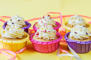 Four multi-colored cupcakes with cream on a yellow background with different ribbons. Festive background with free space. Holiday baking. Birthday baking.