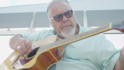 Sunshine flares as a senior man plays on his guitar at home, in slow motion