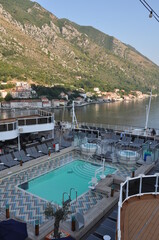 The deck of a cruise ship with a swimming pool and sun beds, against the backdrop of the Adriatic sea off the coast of Montenegro.
