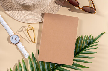 Summer vacation work and travel flat lay. Palm leaves, straw hat, sunglasses and notebook with blank kraft paper cover. Space for notepad print