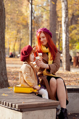 Cheerful and smiling ginger young adult mother in the park having fun with little daughter