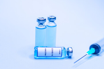Coronavirus vaccine in glass vials with a syringe on a blue background.