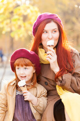 Cheerful and smiling ginger young adult mother in the park having fun with little daughter