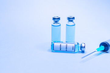 Coronavirus vaccine in glass vials with a syringe on a blue background.