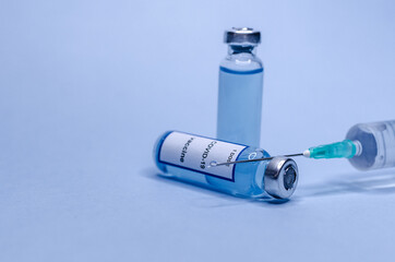 Coronavirus vaccine in glass vials with a syringe on a blue background.