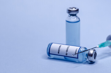 Coronavirus vaccine in glass vials with a syringe on a blue background.