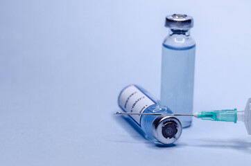 Coronavirus vaccine in glass vials with a syringe on a blue background.