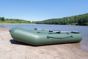 An inflatable rubber boat stands on the banks of a river or lake surrounded by forest. Sunny daytime summer landscape. Background for river walks on water or a concept for fishing. Alone with nature.