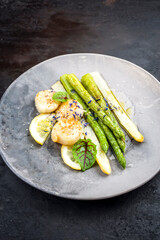 Traditional barbecue scallops with green and white asparagus and butter sauce offered as close-up on a modern design plate