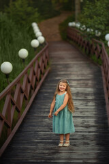A little girl with long hair is jumping on a wooden bridge on the river. Image with selective focus.