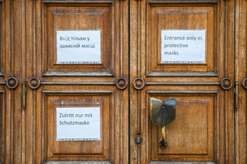 Entrance only in protectrive masks A4 printed warning information on a ancient wooden door
