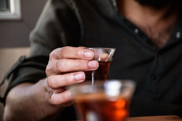 a man holding a cup of turkish tea, hands only - second tea glass in blur foreground.