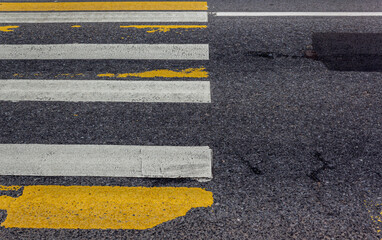 Fototapeta premium Close-up of white and yellow stripes marking a pedestrian crosswalk. Security concept on road, large crosswalk. White and yellow road marking. Zebra crossing. Frayed stripes. High quality photo
