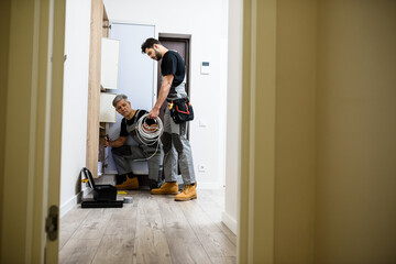 Full length shot of aged electrician, repairman in uniform working, installing ethernet cable or router in fuse box while his young colleague bringing cable