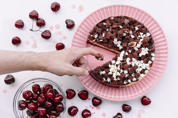 Hand eating cherry and chocolate cake on plate