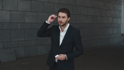 Businessman putting on wireless earphones at street. Man using bluetooth earbuds