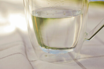 Transparent cup with water on table. Green garden background. Copy space