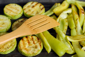 Grilled vegetables in a pan. Close-up of zucchini and sweet peppers. Wooden spatula for cooking