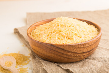 Wooden bowl with raw golden rice and wooden spoon on a white wooden background. Side view, selective focus.