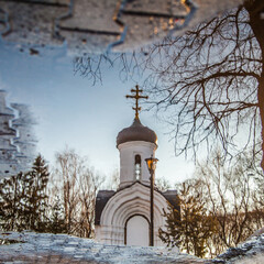 refection of white orthodox chapel in freezing puddle