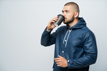 Naklejka premium a man drinks coffee dressed in a blue raincoa