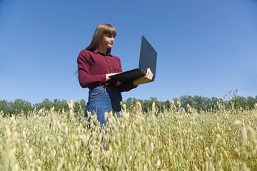 Naklejka na ściany i meble A young girl with a computer in her hands in a farmer's field.
