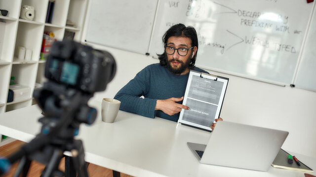 Young professional computer programming teacher recording video blog, explaining java basics online, working from home. Focus on a man