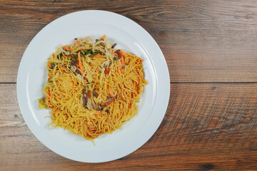 Simple chicken chow mein meal on a white plate and on a wooden table. Chinese style tasty noodles with sauce and vegitables. Concept dinner,  Asian flavor.