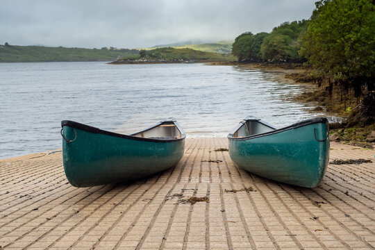 Two blue canoe on rump to water. Nobody. Cloudy sky. Water sports and activity concept.