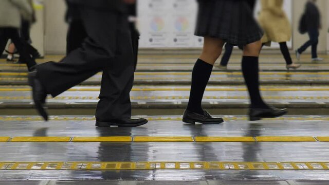 Schoolgirl and office man walk at railway station platform, slow motion shot of legs. Japanese commuters come to train at end of weekday. Passengers seen on background