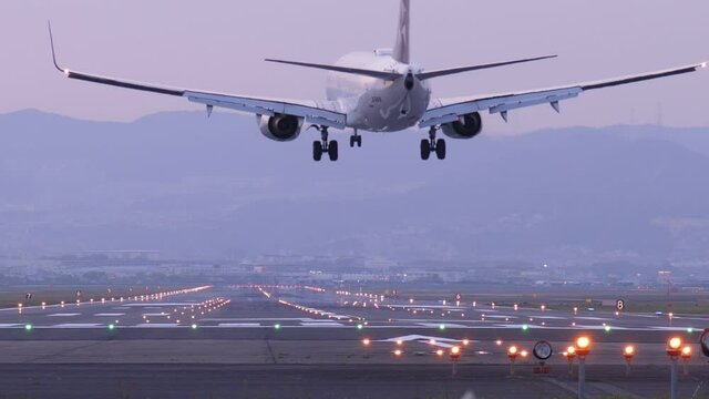 Slow motion shot of landing jet liner, rear view from end of runway. Passenger plane fly down and touch ground. Evening time shot of Itami Airport air traffic
