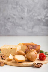 Smoked cheese and various types of cheese with rosemary and tomatoes on wooden board on a gray and white background . Side view, copy space.