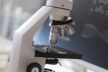 A microscope in a modern laboratory with a medical screen behind.