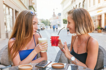 Two female friends drinking lemonade, talking and having fun outdoors