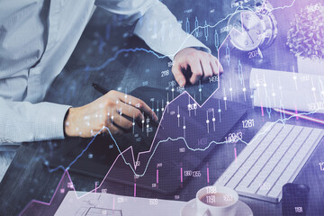 Double exposure of man's hands holding and using a phone and financial graph drawing. Analysis concept.