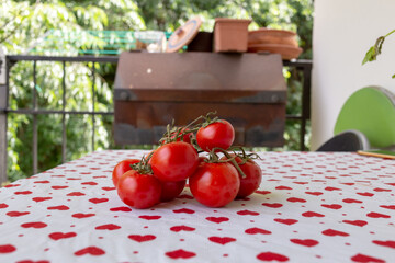 Truss tomatoes on the table with hearts textured table cloth. Rusty Barbecue in the background. Front View.