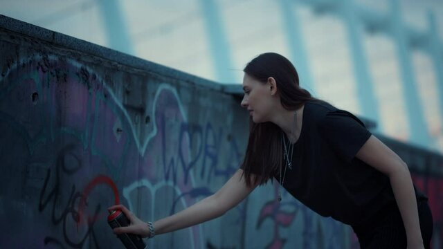 Girl painting graffiti on urban street. Woman using spray bottle for graffiti