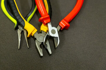 open pliers construction tools with multicolored handles red yellow on a dark background