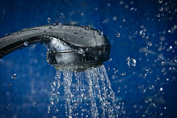 Obraz na płótnie Canvas Shower head against blue wall of bathroom with water drops flying by.